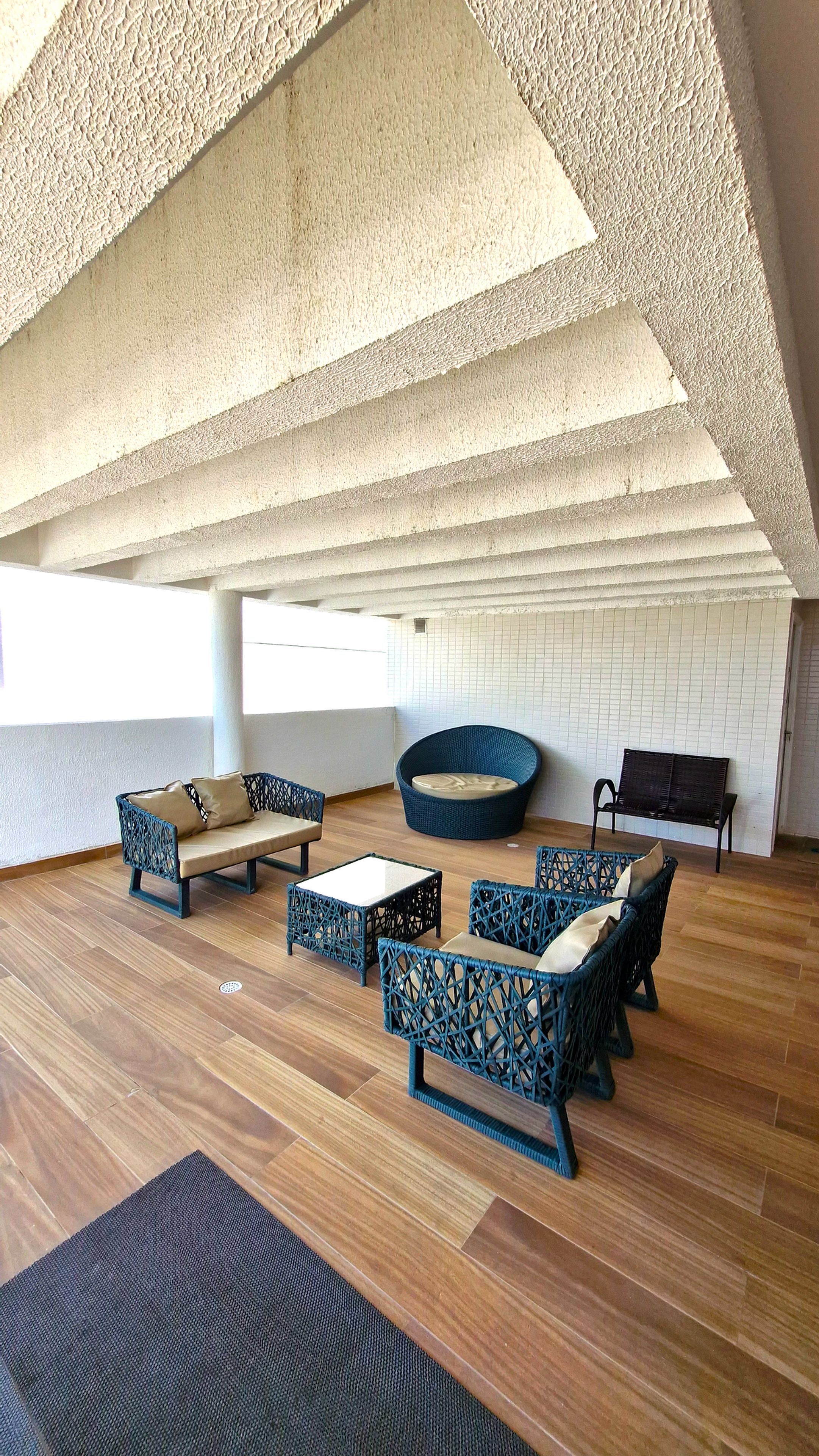 Amplo espaço interno com teto alto, piso de madeira e disposição de assentos incluindo sofá, cadeiras e um banco.