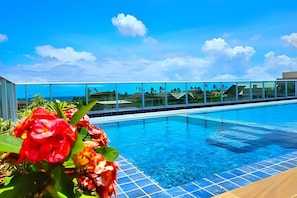 A swimming pool with clear blue water, surrounded by a glass railing, and a view of the ocean in the background. - Cupe Garden - Estúdio Superior (Ipojuca)