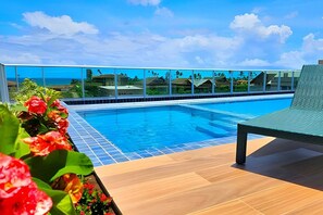 Zona de piscina con vista despejada al océano, una silla de descanso y un deck de baldosas.