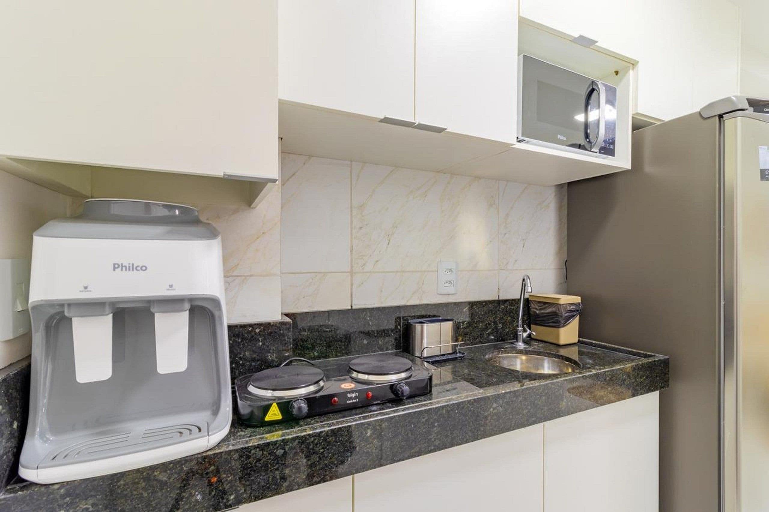 A kitchen with a water dispenser, a stove, a microwave, and a refrigerator.