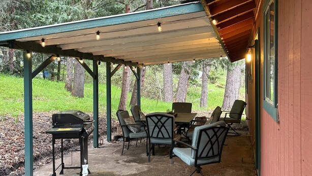 An outdoor patio with a covered seating area, a grill, and a view of the surrounding forest. - Bigfoot Lodge Yosemite Bass Lake (Oakhurst)