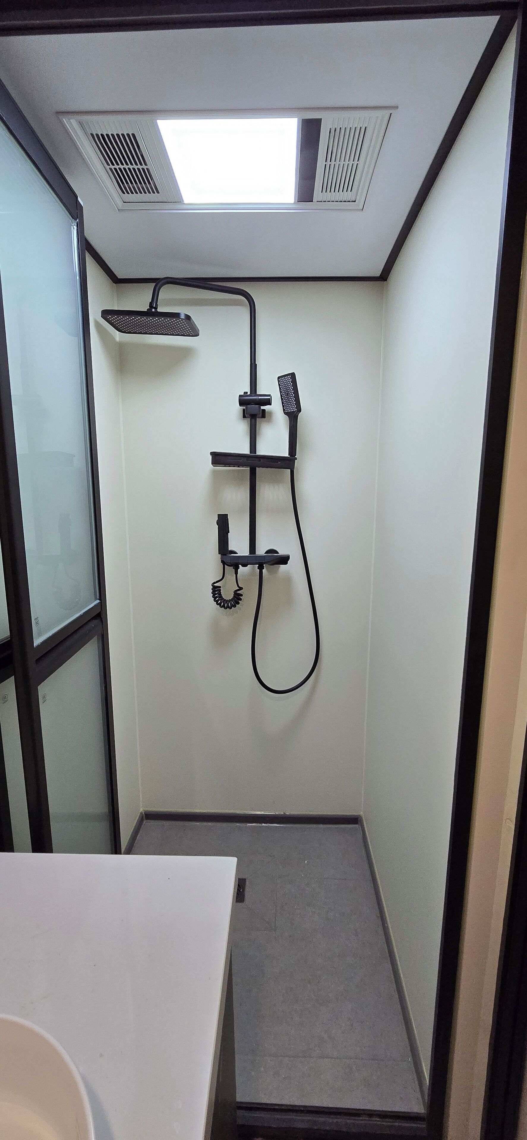 A compact shower area with a handheld showerhead, a wall-mounted faucet, and a ventilation system above.