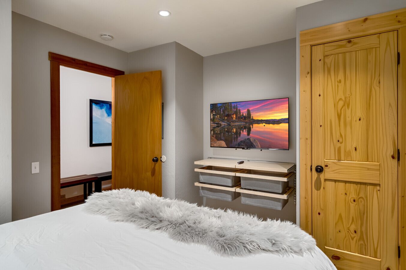 Un dormitorio con una cama, una puerta de madera, un cuadro y un televisor sobre un mueble de madera.