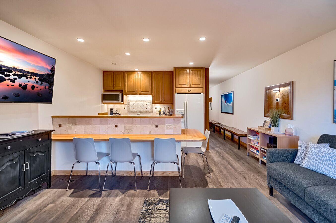 A modern kitchen with a central island, wooden cabinets, and a dining area with chairs.