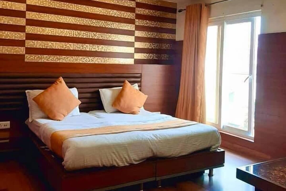 A modern hotel room with a large bed, wooden flooring, a ceiling fan, and a large window with curtains.