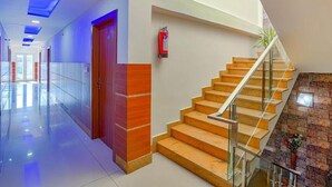 A modern hotel lobby with a glass corridor, a wooden door, a staircase with glass railings, and a fire extinguisher mounted on the wall. - Hotel 24x7 Inn (Jalandhar)