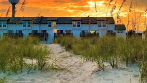 A row of beach houses with a water tower in the background, surrounded by sand and grass.