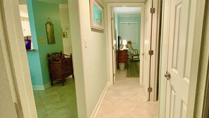 A hallway with a green carpet, a wooden dresser, a rocking chair, and a door with a light switch.