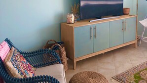 A living room with a sofa, a television on a cabinet, a woven ottoman, and a floor lamp.