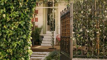 A garden entrance with a stone wall, a metal gate, and a pathway leading to a building with a green door.