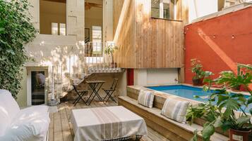 A wooden deck with a pool, outdoor seating, and a staircase leading to an upper level.