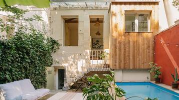 A courtyard with a pool, a wooden deck, a white sofa, and a small staircase leading to an upper level.