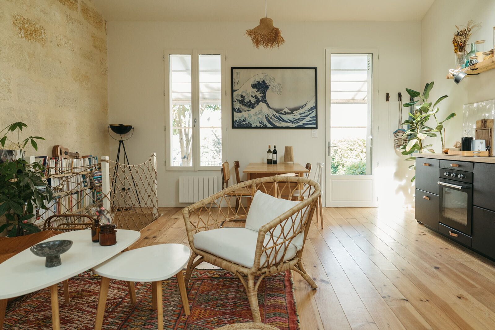 Un coin repas chaleureux avec des chaises en osier et une table, une cuisine équipée d’une cuisinière, et un grand tableau accroché au mur.