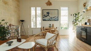 A cozy dining area with wicker chairs and a table, a kitchen with a stove, and a large painting on the wall. - Charming renovated house with small pool in the La Bastide district (Bordeaux)