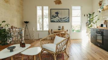 Un coin repas chaleureux avec des chaises en osier et une table, une cuisine équipée d’une cuisinière, et un grand tableau accroché au mur.