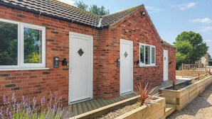 A brick house with two white doors, a wooden deck, and a garden with lavender plants. - 1 bedroom accommodation in Walcott (Walcott)