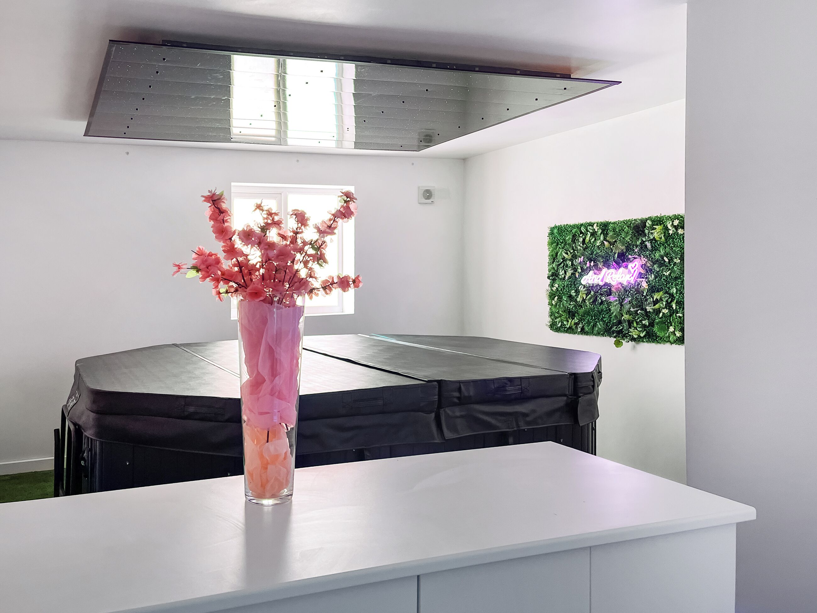 A room with a white table, a black sofa, a window, and a green wall decoration.