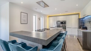 A modern kitchen with a central island, bar stools, stainless steel appliances, and a framed quote on the wall. - The Old School House (Barnsley)