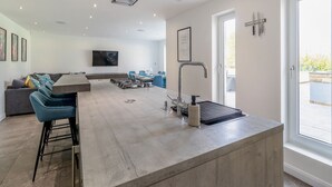 A modern kitchen with a central island, bar stools, a flat-screen TV, and a dining area with chairs. - The Old School House (Barnsley)