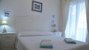 A neatly made bed with two folded towels, a white nightstand with a lamp, and a framed picture on the wall.