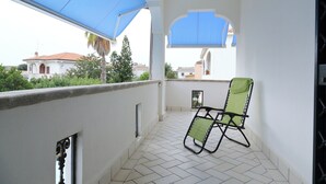 A balcony with a tiled floor, a chair, and a blue awning.