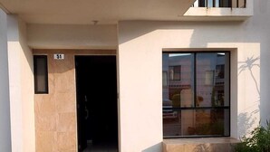 A modern building with a paved entrance, a visible door, and a window with a view of other buildings.