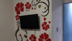 A room with a mounted TV on the wall, an air conditioning unit above it, and a door to the right.