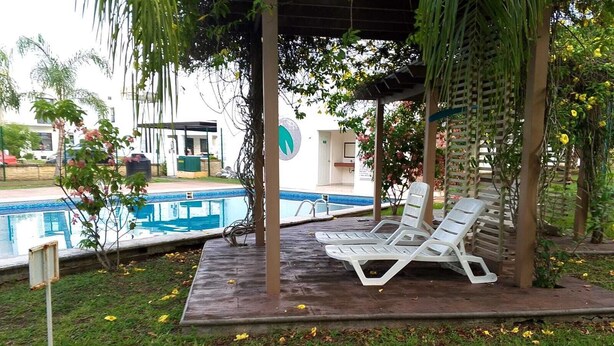 A covered pool area with two white lounge chairs and a small pool.
