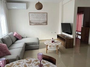 A modern living room with a grey sofa, a small round table with a wine glass, a flat-screen TV on a wooden stand, and a decorative wall piece. - Sweet Home Mitropoleos (Kastoria)