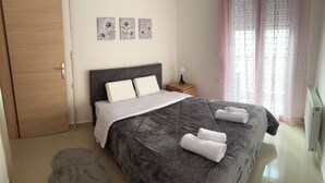 Ein Schlafzimmer mit Bett, Kissen, Nachttisch, Lampe, Heizkörper und einem Fenster mit Vorhängen.