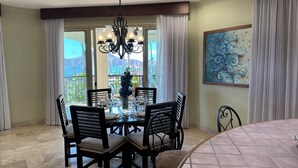 A dining area with a glass table, black chairs, a chandelier, and a view of the sea.