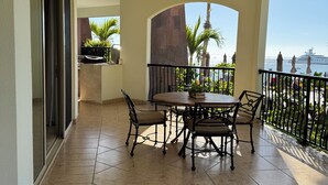A covered patio area with a round table and chairs, a ceiling fan, and a view of the sea and a yacht.