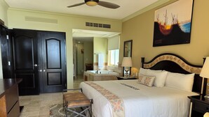A hotel room with a large bed, a desk, a chair, a bathroom visible through an open door, and a painting on the wall.