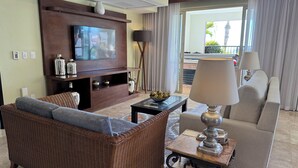 A living room with a television, wicker furniture, a coffee table, and a lamp.