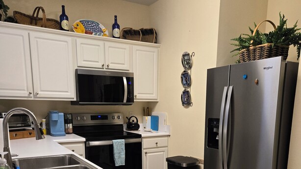 A modern kitchen with white cabinetry, a stainless steel refrigerator, a microwave, and a sink. - Sandpiper Bay 3rd Floor. 4 mi to beach. 3 bd, 2 ba, new kitchen,  pool & more (Sunset Beach)