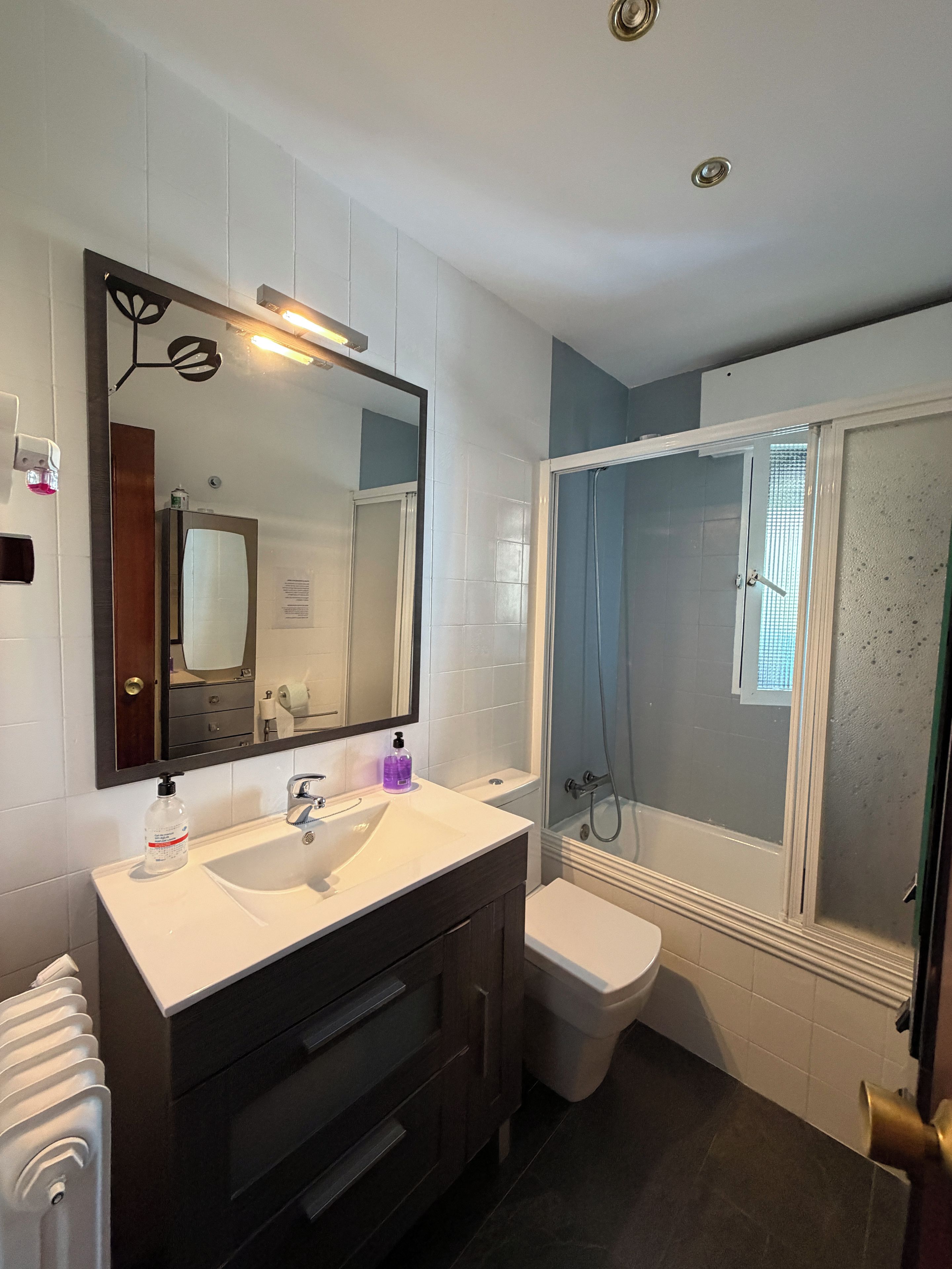 Un baño con un lavamanos blanco, tocador de madera oscura, un espejo grande, cabina de ducha y un inodoro.