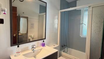 Un baño con un lavamanos blanco, tocador de madera oscura, un espejo grande, cabina de ducha y un inodoro.