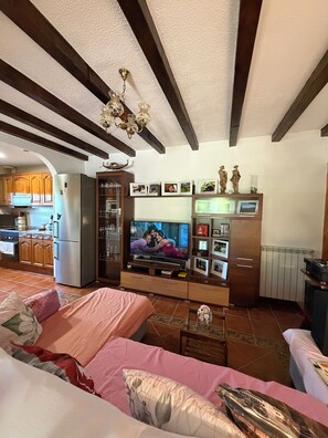 Un soggiorno con televisione, mobili in legno e una cucina sullo sfondo.