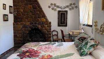 Ein Schlafzimmer mit Kamin aus Stein, einem Bett mit floralem Bettbezug, einem Deckenventilator und einer Essecke mit Tisch und Stühlen.