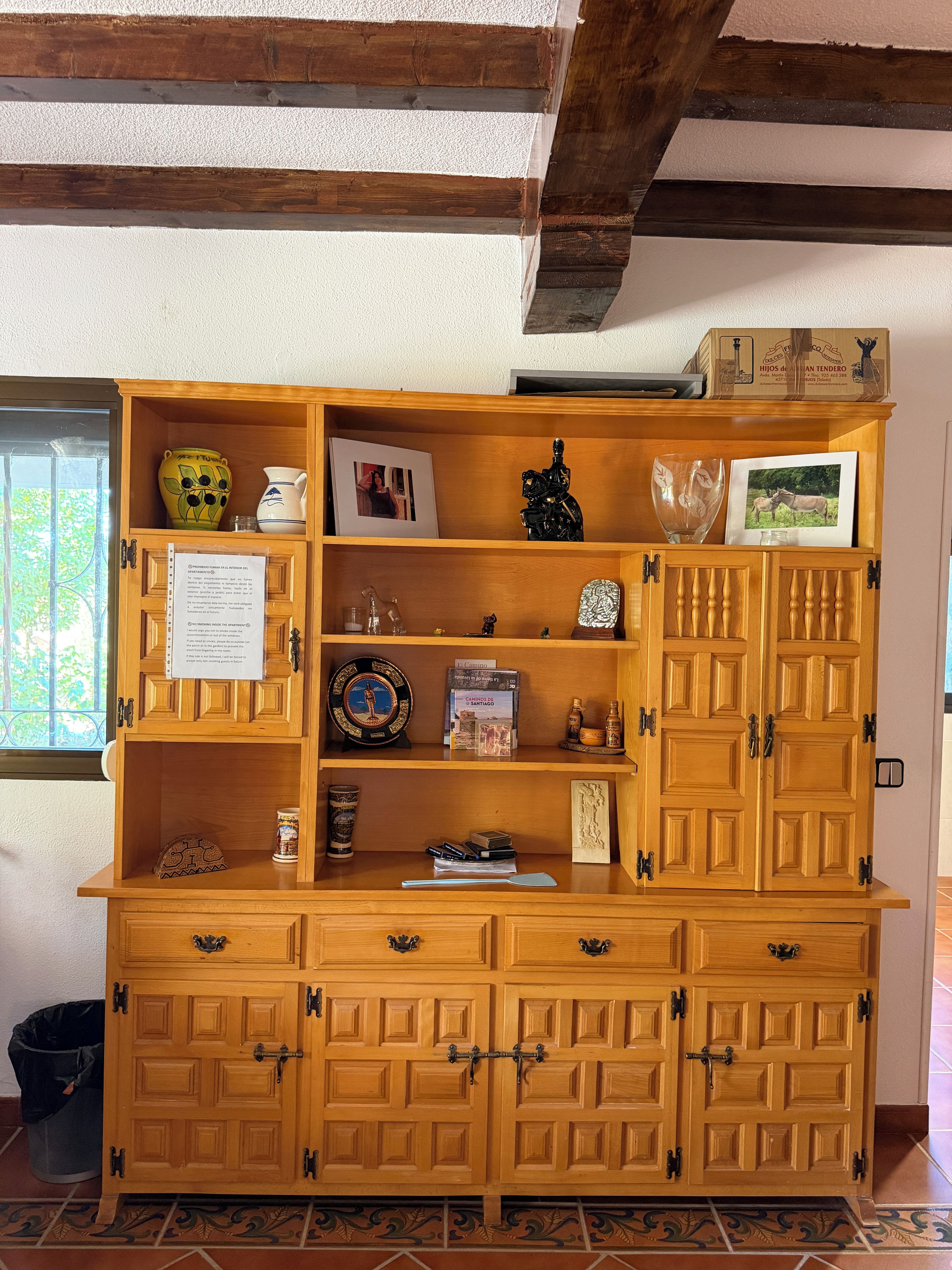 Un mueble de madera con varios estantes y cajones, que contiene objetos como libros, adornos y fotografías enmarcadas.