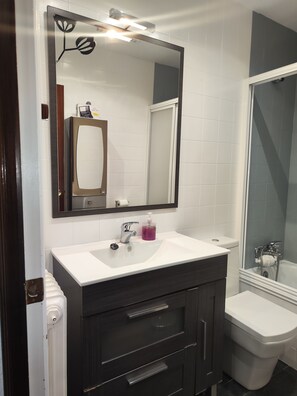 A bathroom with a white sink, dark wooden vanity, a mirror, and a shower area.