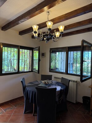 Un'area pranzo con un lampadario, ampie finestre vista su vegetazione e un pavimento piastrellato.