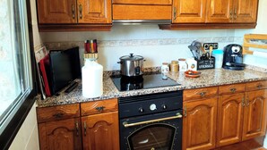 A kitchen with wooden cabinets, a stove, a microwave, and various kitchen utensils. - Campo cerca de Madrid – Kids & pets welcome (Sotolargo)