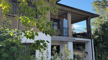 Een gebouw met twee verdiepingen en een balkon, omgeven door groen.