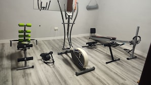 Un gimnasio en casa con cinta de correr, elíptica, banco de pesas y diverso equipo de ejercicio.