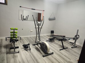 Un gimnasio en casa con cinta de correr, elíptica, banco de pesas y diverso equipo de ejercicio.