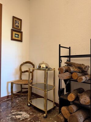 Una stanza con una sedia in legno, un comò con specchio dorato e uno scaffale con legna da ardere.