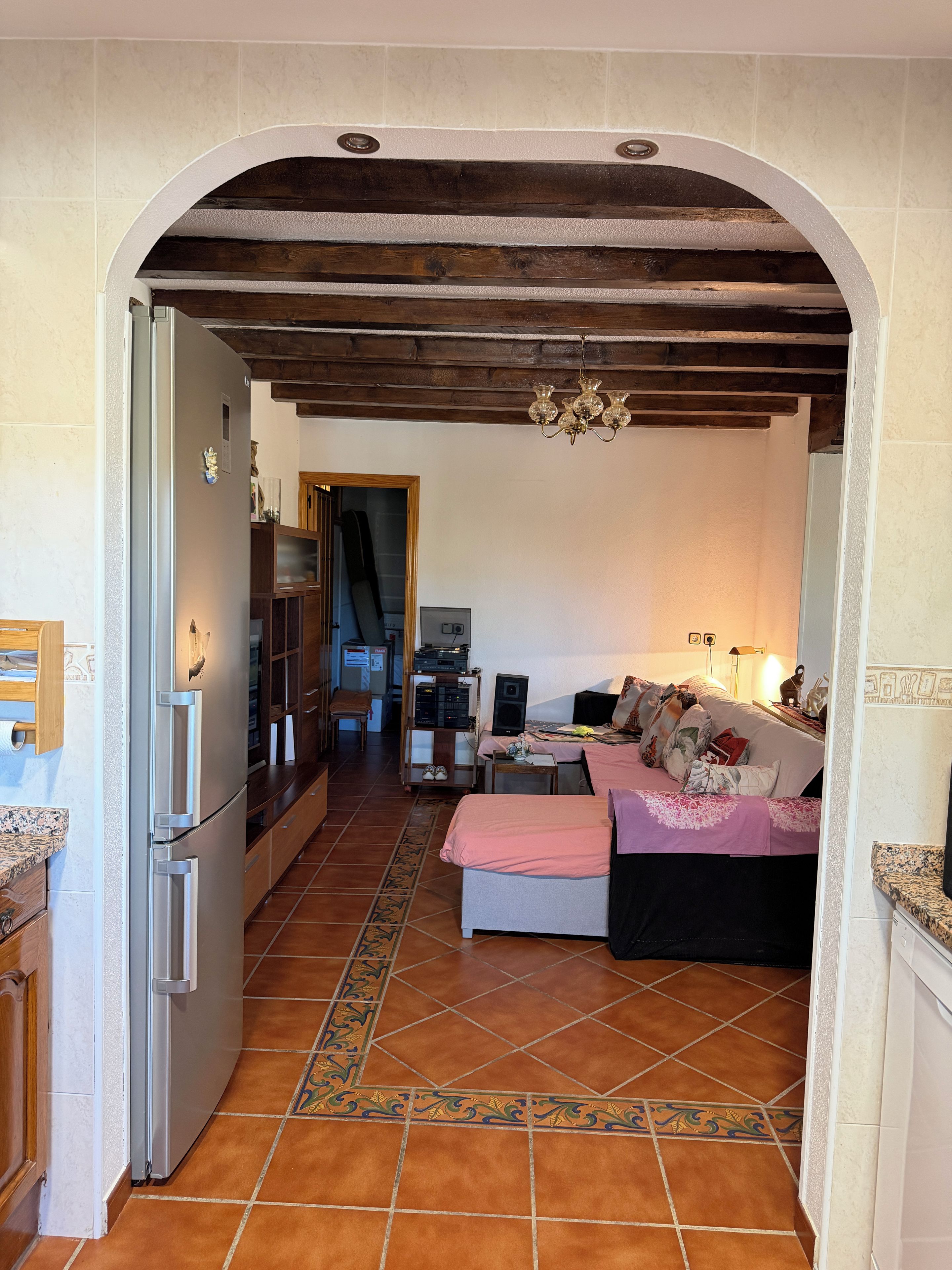 Una cocina con refrigerador, un comedor con mesa y sillas, y una sala de estar con sofá y televisor.
