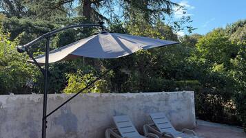 Un espace patio avec un parasol, deux chaises longues et un sol en briques.