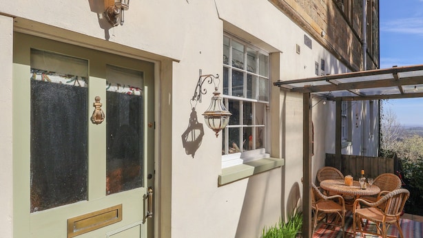 A quaint house with a green door, a small balcony with wicker furniture, and a view of the countryside. - Church Garden Apartment (Malvern)